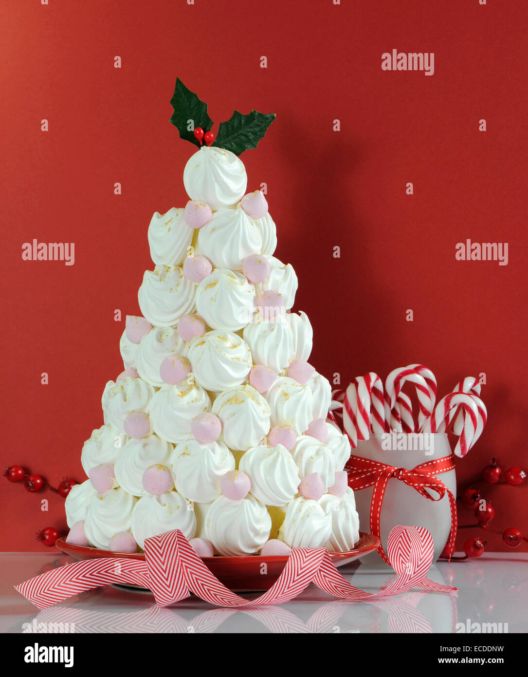 Árbol de Navidad hecho con Dessert Treat merengues rosados y blancos con decoraciones de bastón de caramelo contra un fondo de color rojo. Foto de stock