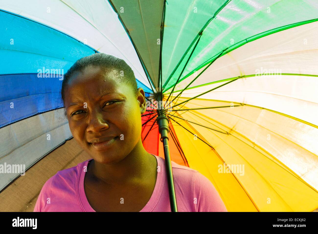 Mauricio, la Isla Rodrigues, Port Mathurin, retrato de una joven mujer Criolla bajo un paraguas arco iris del cielo para protegerse del sol Foto de stock