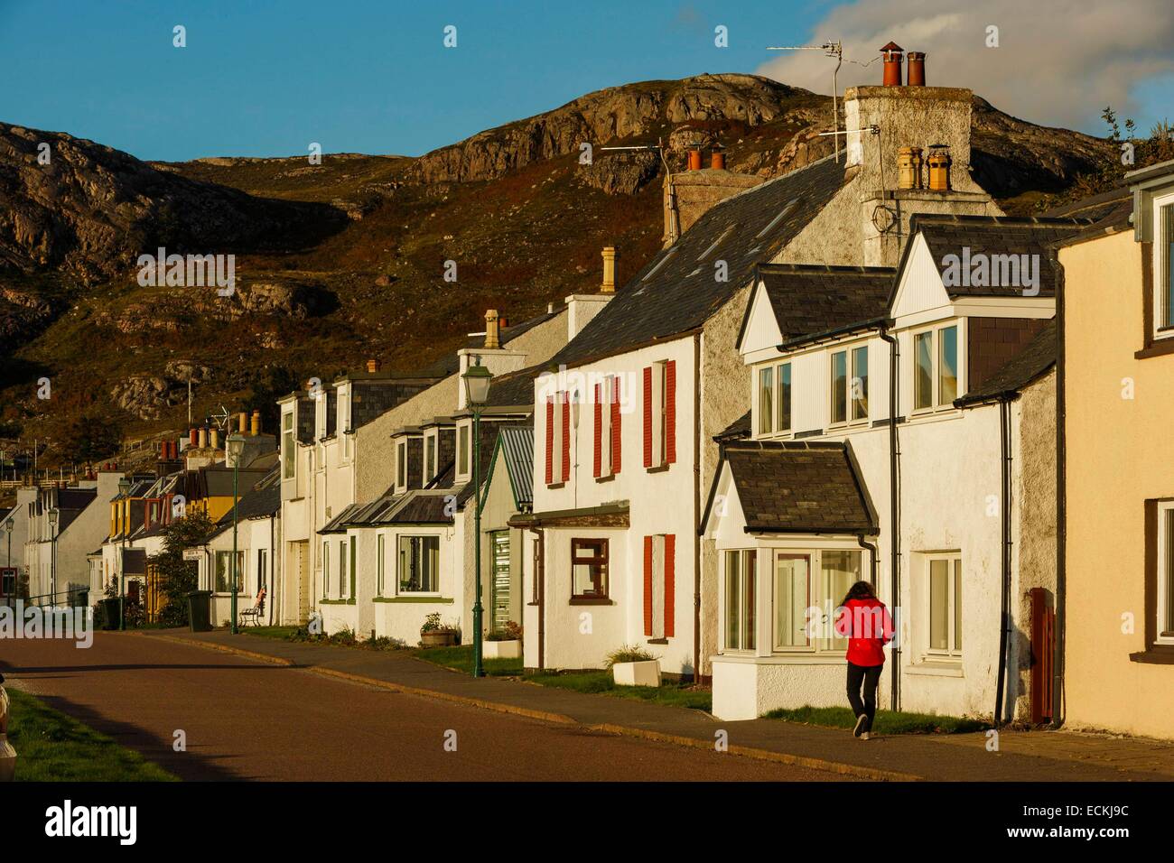 Reino Unido, Escocia, Wester Ross, Shieldaig, vista horizontal de la calle principal de un pueblo de pescadores caminar solamente una mujer en rojo en otoño Foto de stock