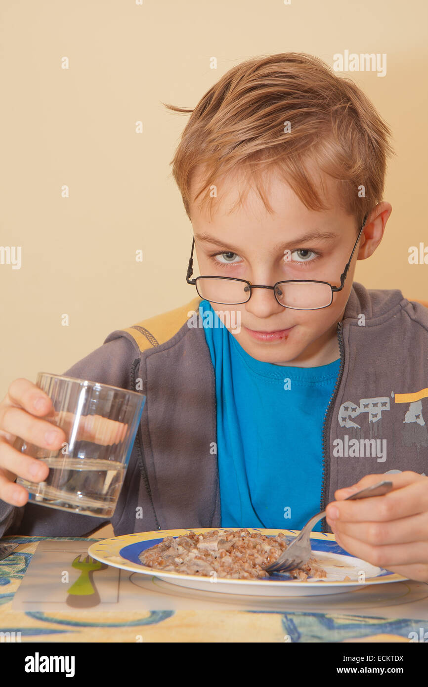 Un pequeño niño está comiendo su comida sentado en la mesa. Foto de stock