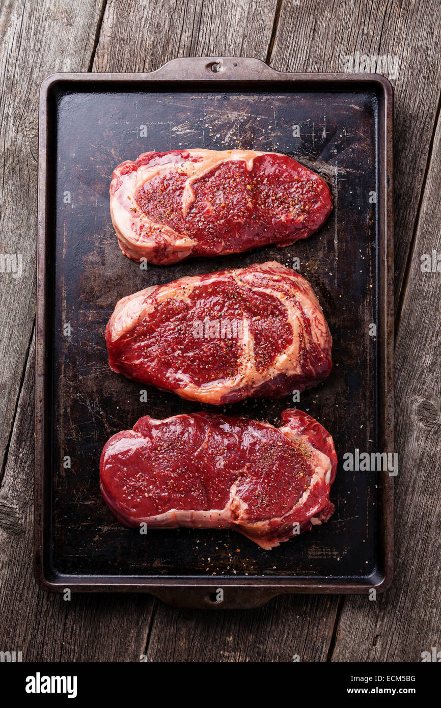 Tres cortes de carne fresca cruda bistecs y condimentos sobre fondo oscuro Foto de stock