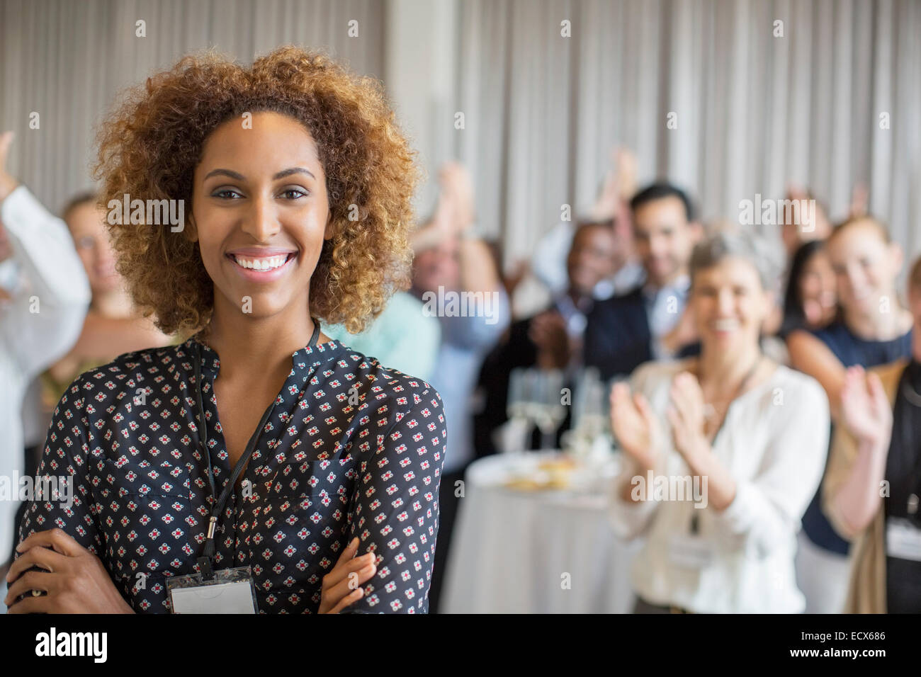 Retrato de mujer sonriente en la sala con la gente aplaudiendo en segundo plano. Foto de stock