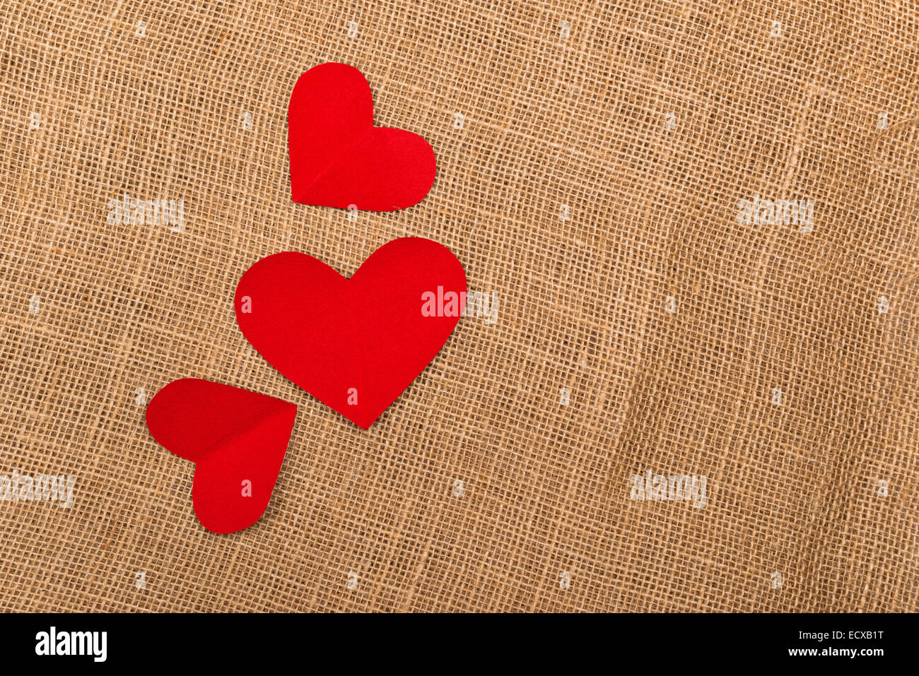 Antecedentes del Día de San Valentín con corazones de papel rojo en arpillera del yute natural textura como espacio de copia. Foto de stock