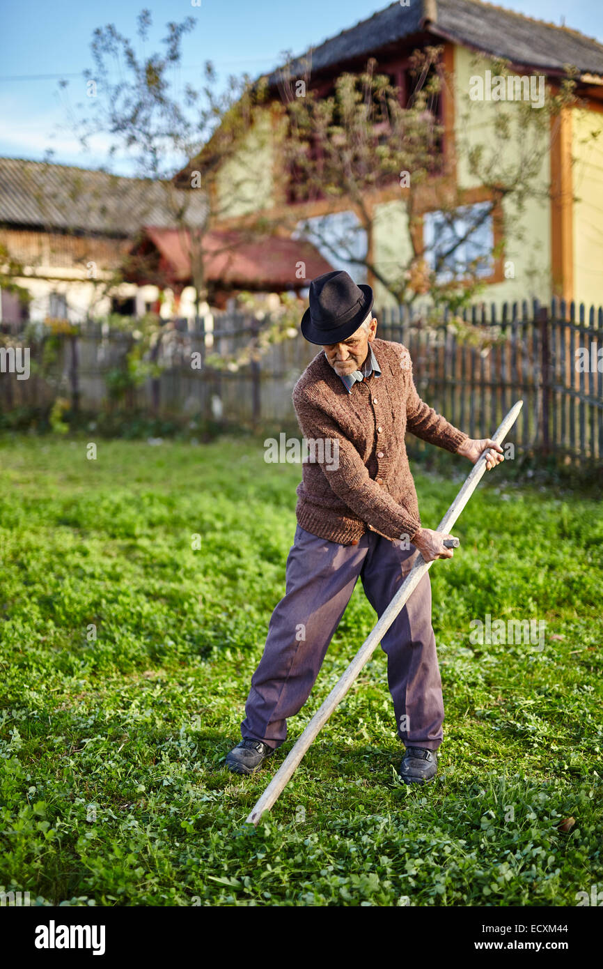 Altos agricultor segando la hierba con una guadaña en el patio de su casa  Fotografía de stock - Alamy