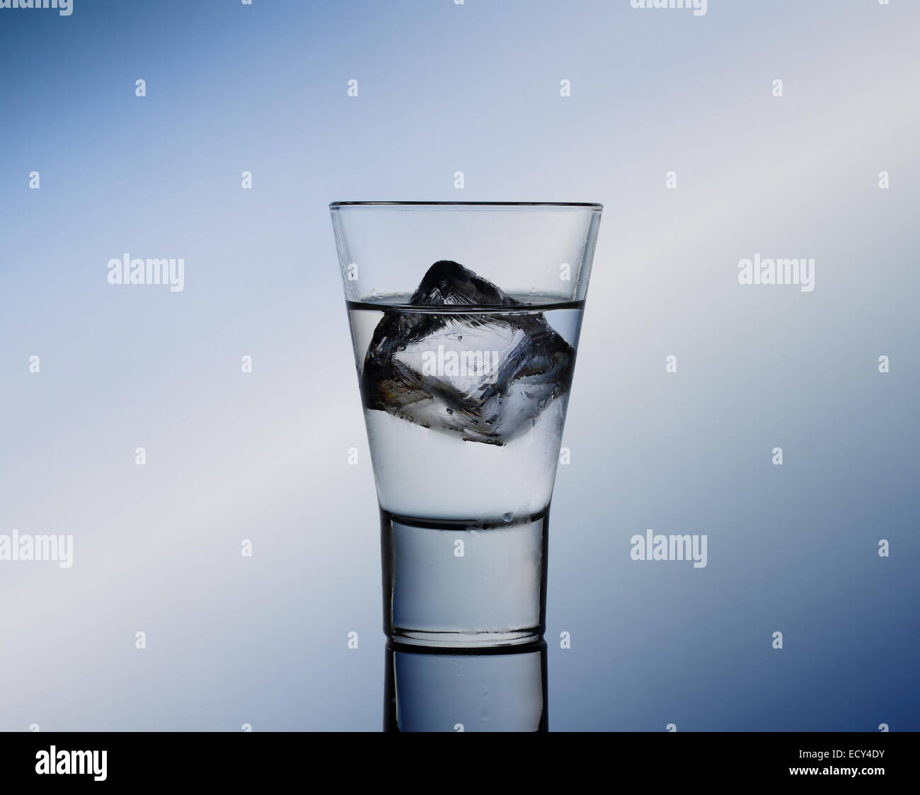 Bebida corta de cristal con líquido claro y cubitos de hielo, fondo azul Foto de stock