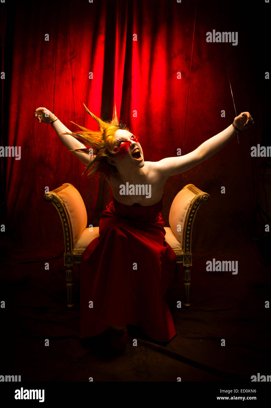 Fantasy makeover fotografía - Seven Deadly Sins - Wrath : una joven chica modelo con puntiagudos alegre cabello hecha para parecerse a una cara blanca de porcelana pintada de títere y posando como una muñeca en un estudio de fotografía vistiendo una levita vestido vestido rojo Foto de stock