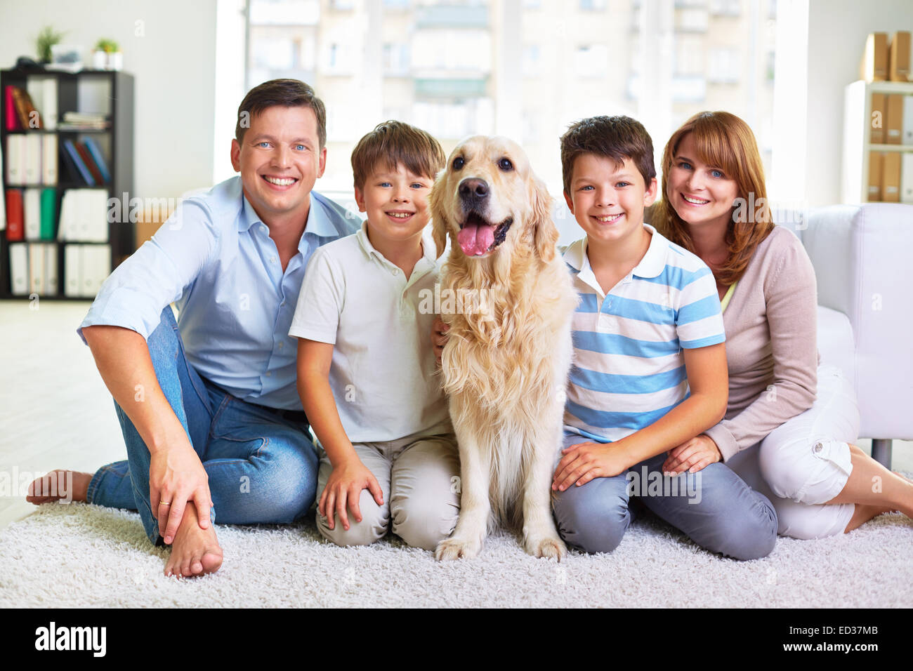 Afectuoso padre, madre, hermanos y esponjosos pet sentado en el suelo Foto de stock