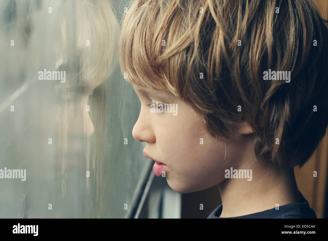 Cute 6 años Chico mirando por la ventana Foto de stock