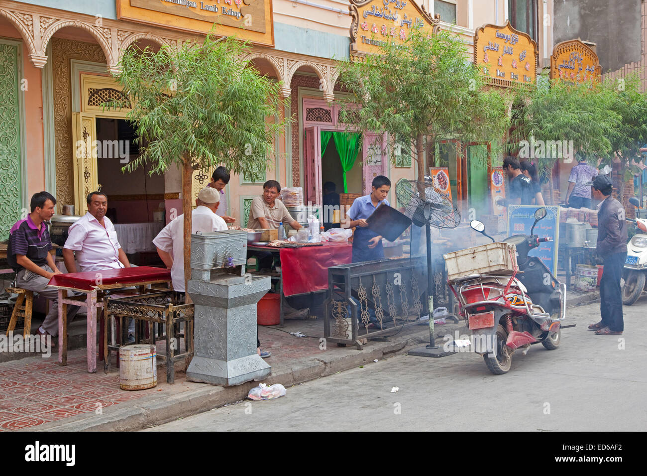 Los hombres uigur comiendo carne asada al aire libre en el pequeño restaurante tradicional en la ciudad de Kashgar / Kashi, La Provincia china de Xinjiang Foto de stock