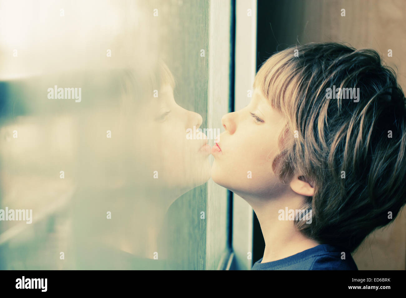 Cute 6 años Chico mirando por la ventana Foto de stock