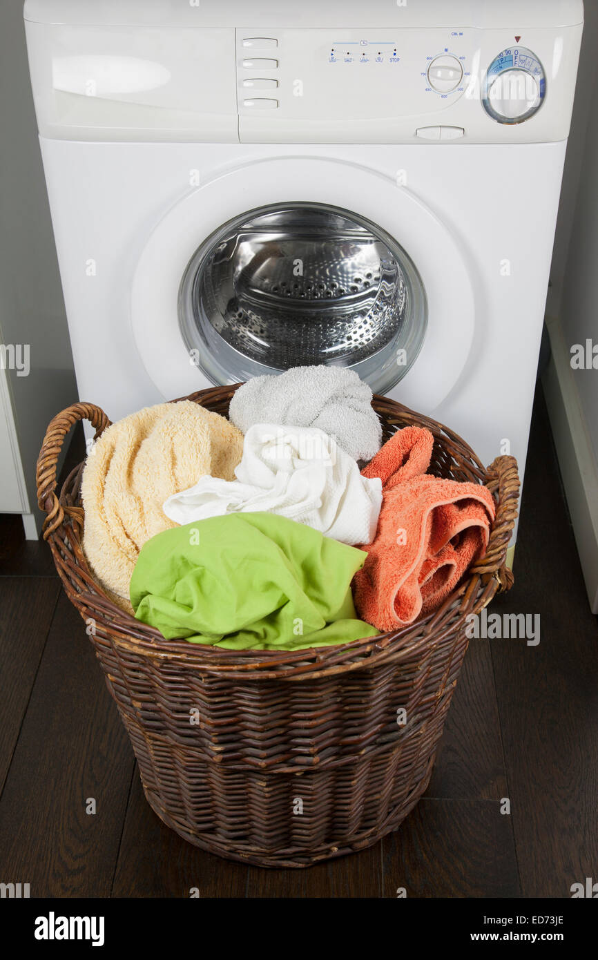 Cesta de mimbre de madera marrón lleno de ropa sucia sábanas y toallas en la puerta lavadora blanca de stock - Alamy