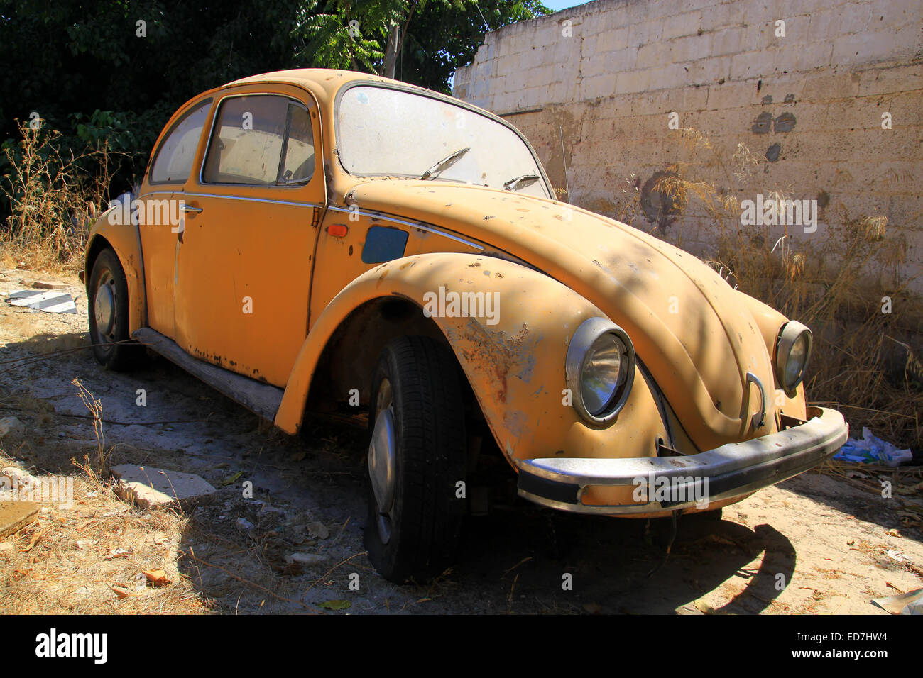 Un viejo coche amarillo está estacionado en un patio abandonado. Foto de stock