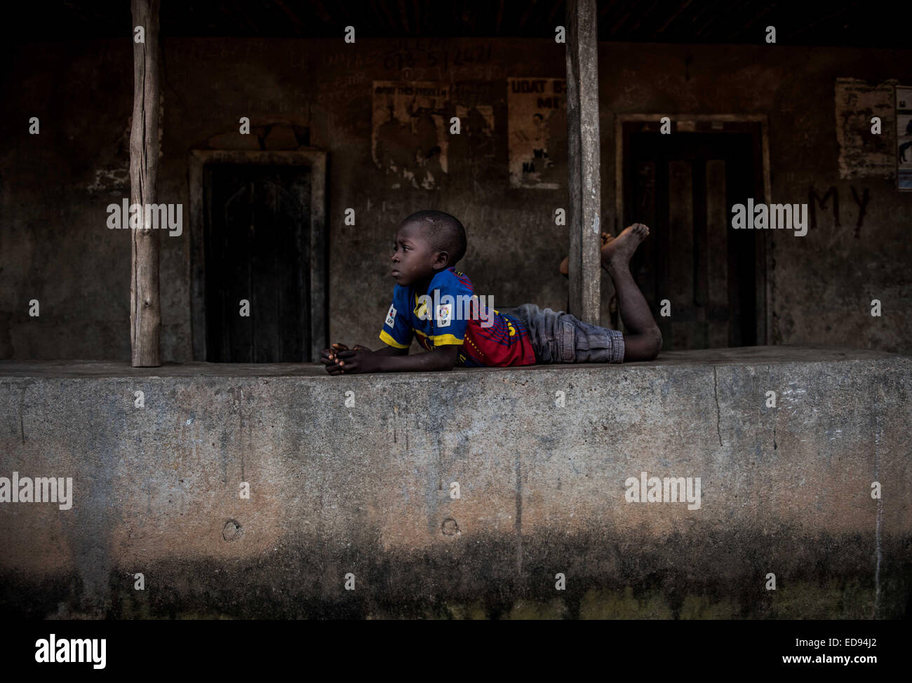 Un muchacho descansa sobre la pared de una casa donde alguien ha muerto recientemente de Ébola. Con el Ébola propagándose a través de las aldeas de los alrededores de Makeni, algunos han conseguido para protegerse a sí mismos, mientras que otros han sido devastadas por el virus. La aldea de Yeli Sanda perdió decenas al virus, mientras que a tan sólo 100 m de la carretera, la vecina aldea Yoni ha evitado por completo. El 28 de noviembre de 2014. Makeni, Sierra Leona. Foto de stock