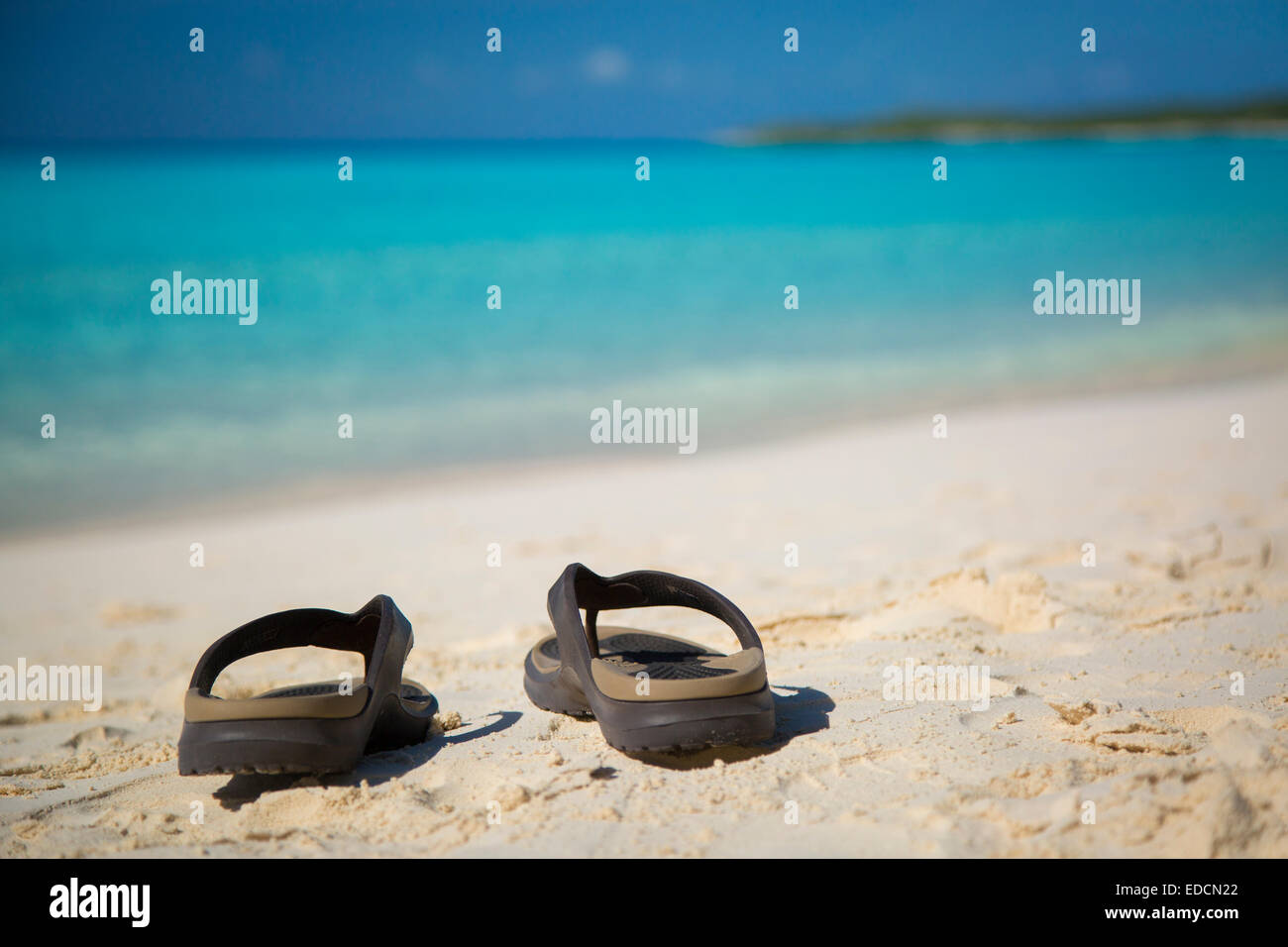 Flip Flops en una playa de arena, con aguas de color turquesa, más allá de la Media Luna Cay, Bahamas Foto de stock
