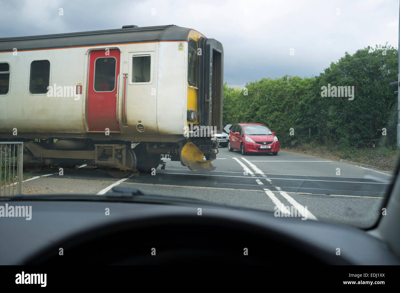 Coches esperando el tren de pasajeros para pasar a nivel unbarriered cruce, Melton, Suffolk, Reino Unido. Foto de stock