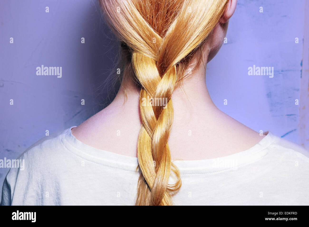Chica con el pelo rubio, trenzado en una trenza sobre un fondo violeta Foto de stock