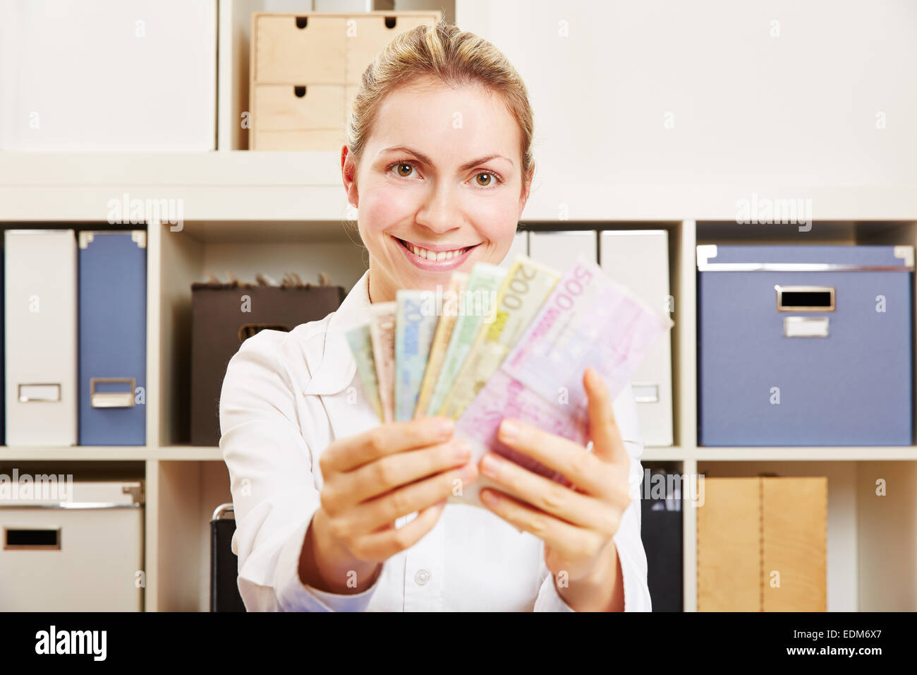 Sonriente joven mujer de negocios con dinero Euro ventilador en su escritorio Foto de stock