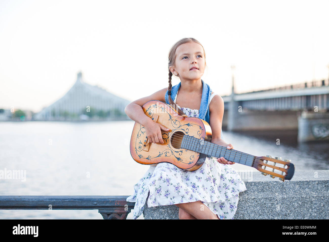 Chica tocando la guitarra en el terraplén del río Foto de stock