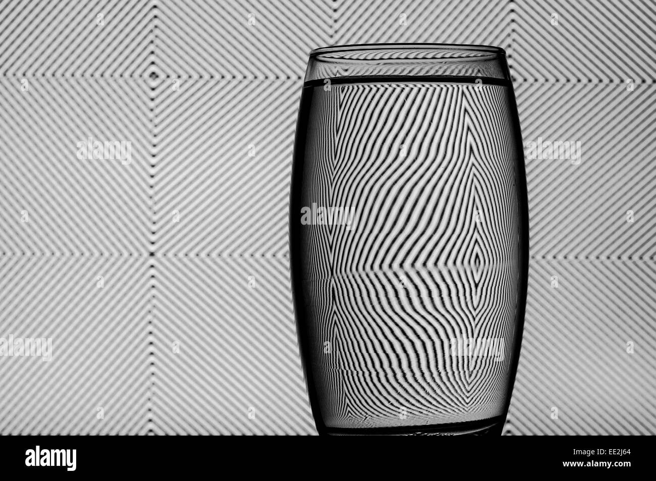 Un vaso de agua contra una trama de fondo para ilustrar el efecto de refracción del agua. Foto de stock