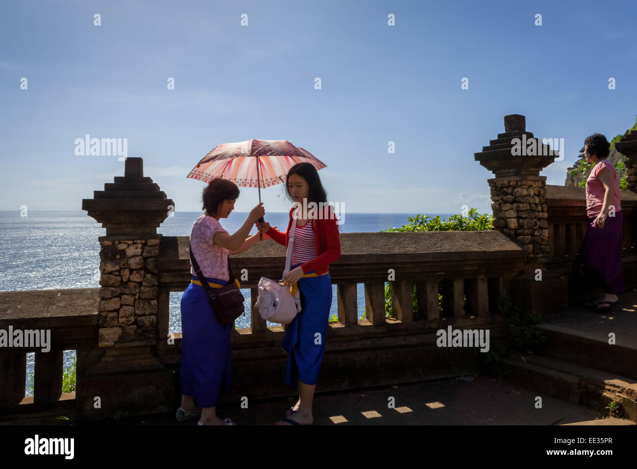 Los turistas de Asia oriental compartiendo un paraguas en un día soleado en Uluwatu, Bali. Foto de stock