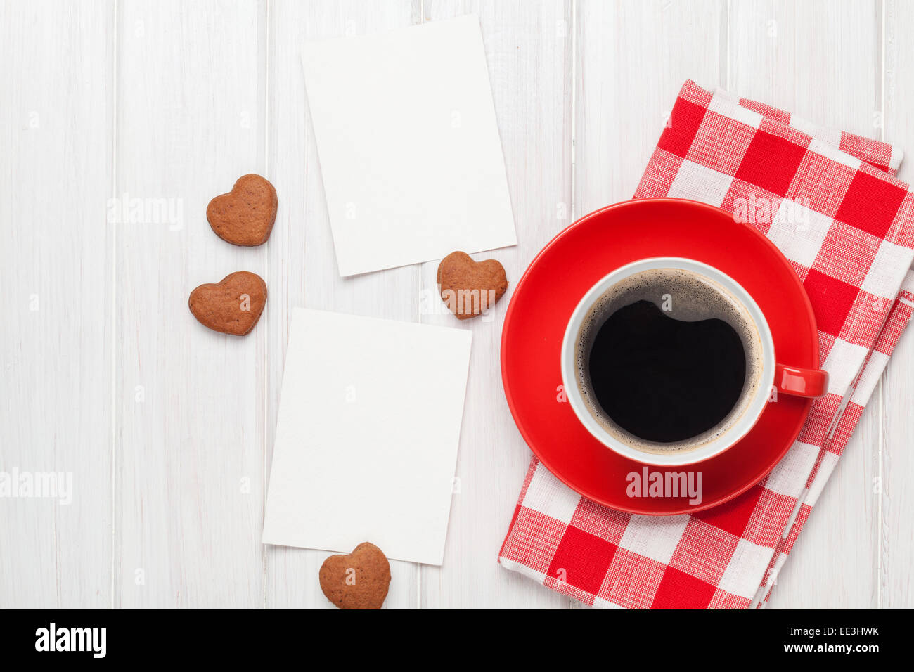 San Valentín en marcos de fotos en blanco, taza de café y galletas en forma de corazón sobre mesa de madera blanca Foto de stock