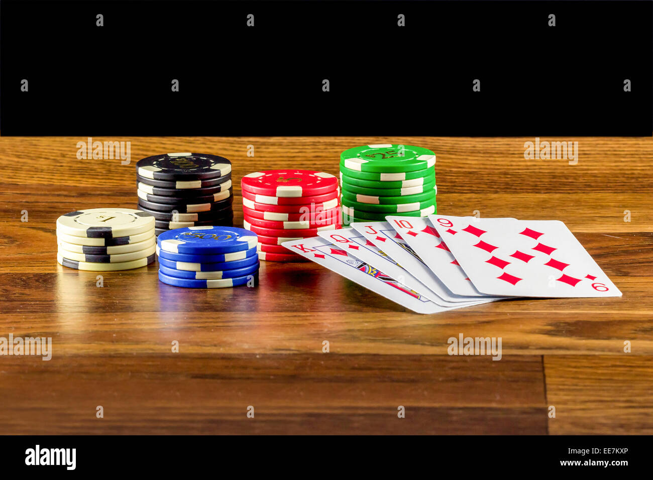 Chips y jugando a las cartas sobre una mesa de madera polvoriento con fondo negro Foto de stock