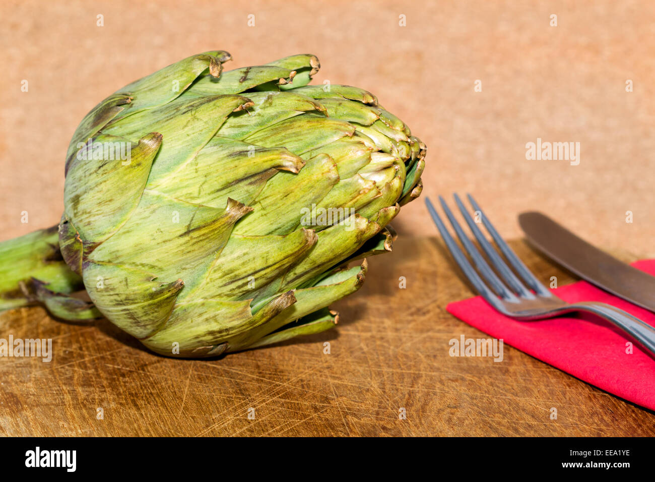 Alcachofa sobre una mesa con cubiertos y servilleta Foto de stock