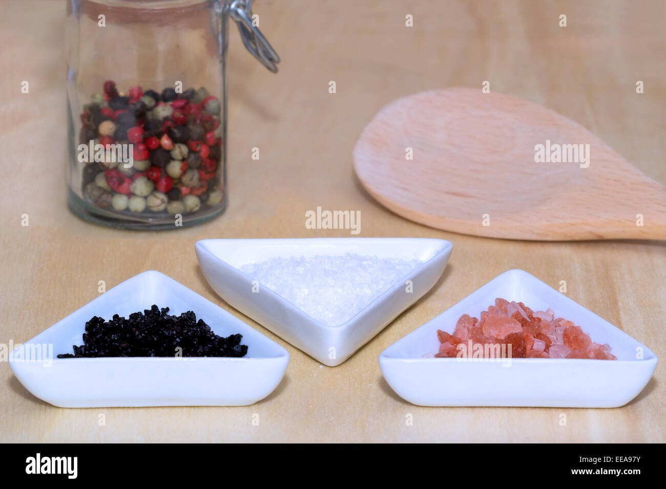 Tres tipos de sal con pimienta de colores y una cuchara de cocina Foto de stock