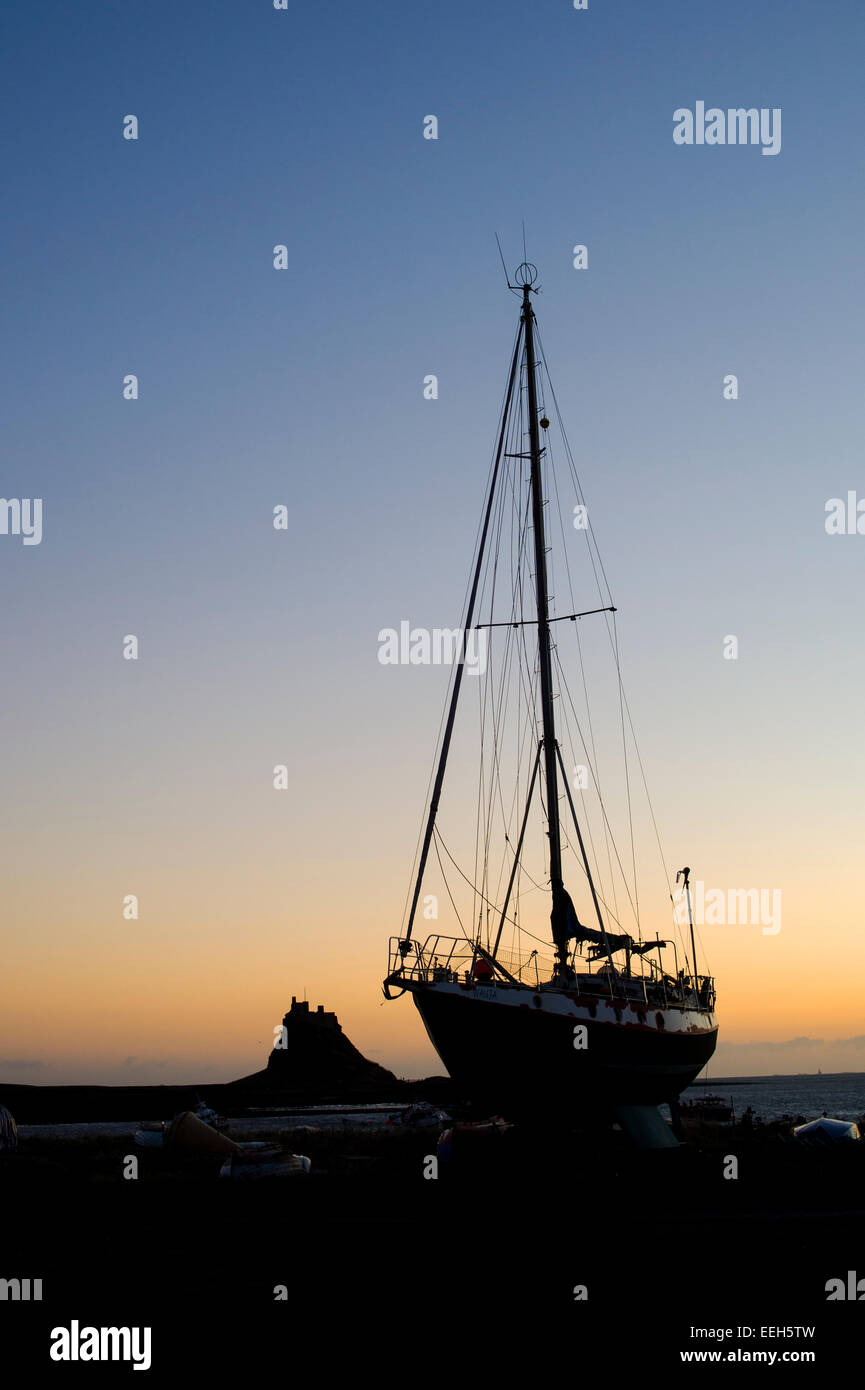 Barco de vela en tierra seca en un amanecer en el puerto, en Lindisfarne, Holy Island, Northumberland, Inglaterra. Silueta Foto de stock