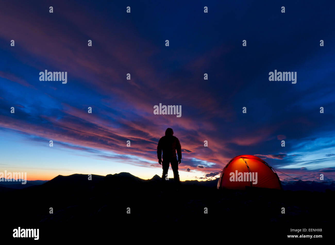 El hombre permanece en el amanecer -iluminado junto a su carpa, Moere und Romsdal Fylke, Vestland, Noruega, Septiembre Foto de stock