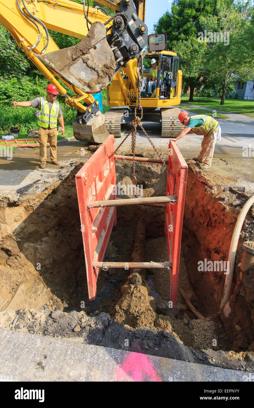Trabajador de la construcción colocando las entibaciones en el agujero con la excavadora Foto de stock