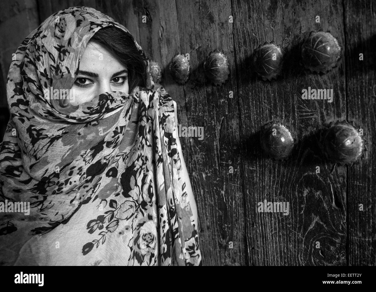 Mujer con hermosos ojos Hidding detrás de un velo delante de una vieja puerta de madera, Koya, Kurdistán, Irak Foto de stock