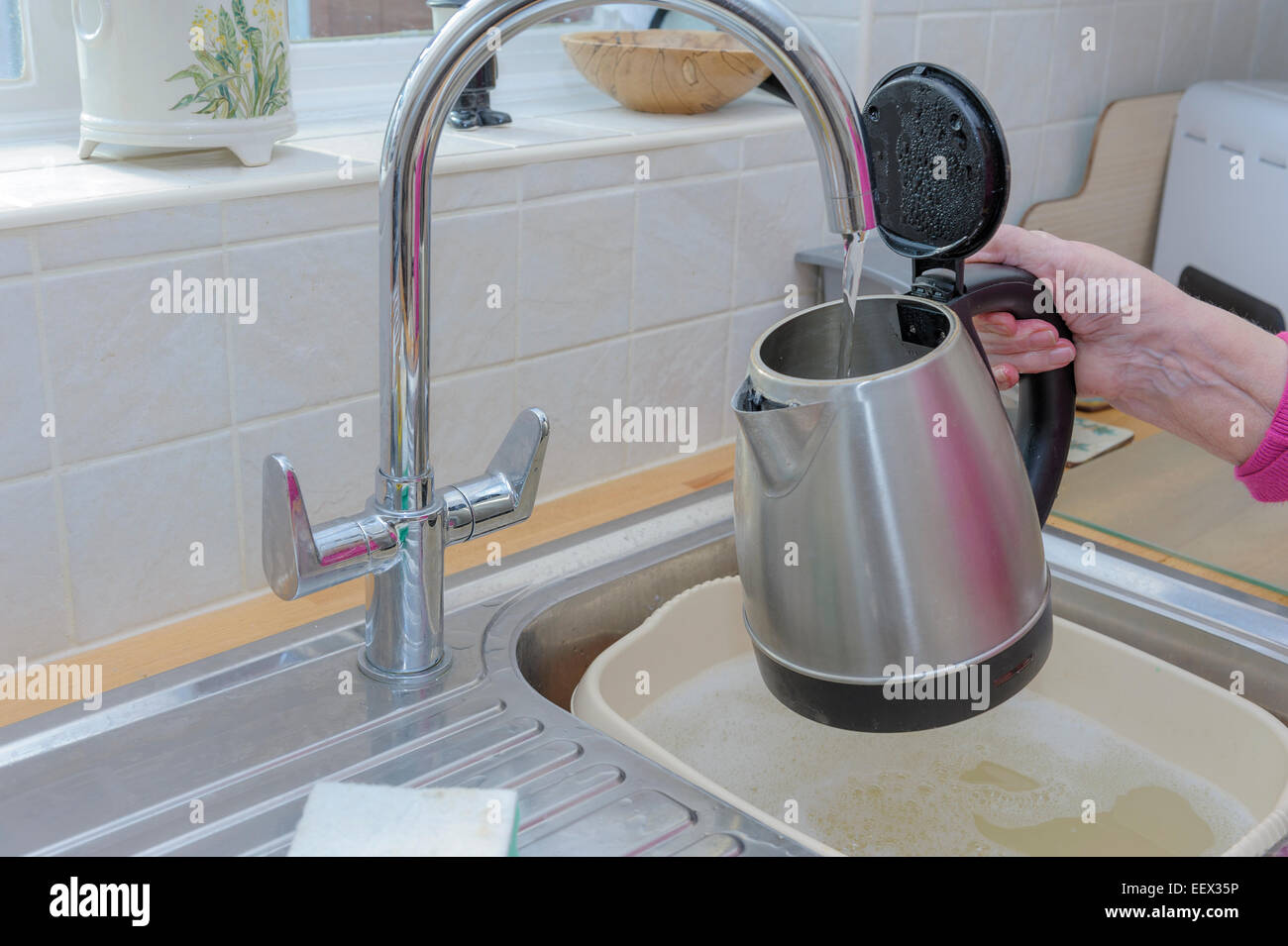 Mostrando ancianos artríticos womans mano sujetando hervidor de agua bajo el grifo de la cocina mientras se llena con agua Foto de stock