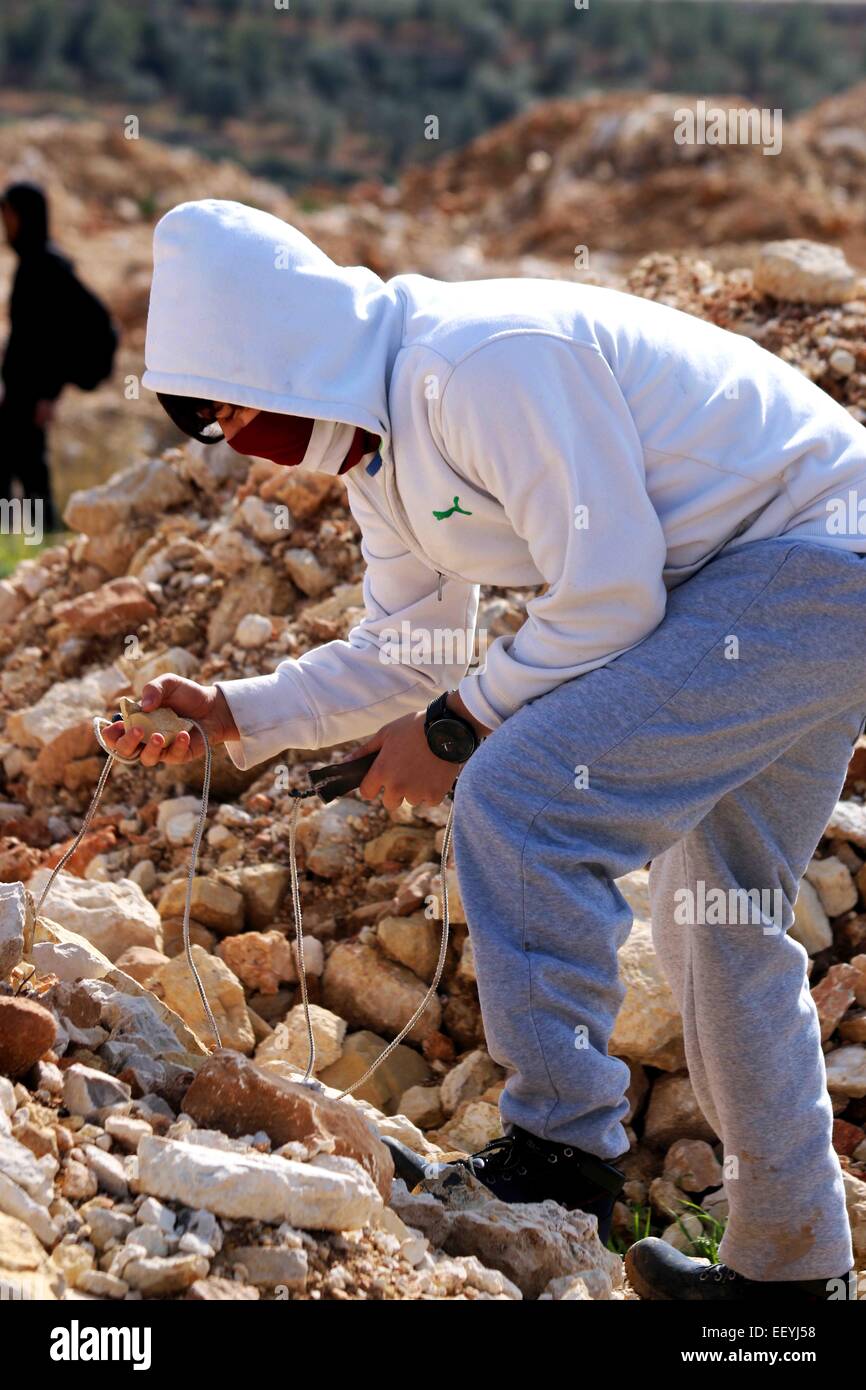 Un joven palestino enmascarada en la aldea de Cisjordania Nabi Saleh gira  sobre una roca en una mano, mientras con un tirachinas casero en otro.  Semanalmente el viernes manifestaciones en contra de