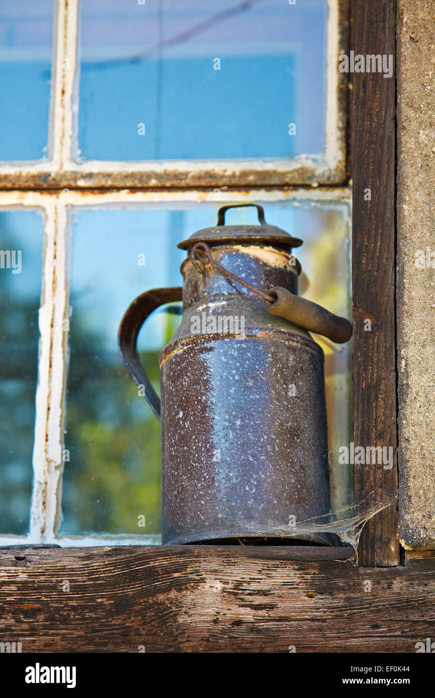 Una vieja jarra de leche en el alféizar de la ventana. Foto de stock