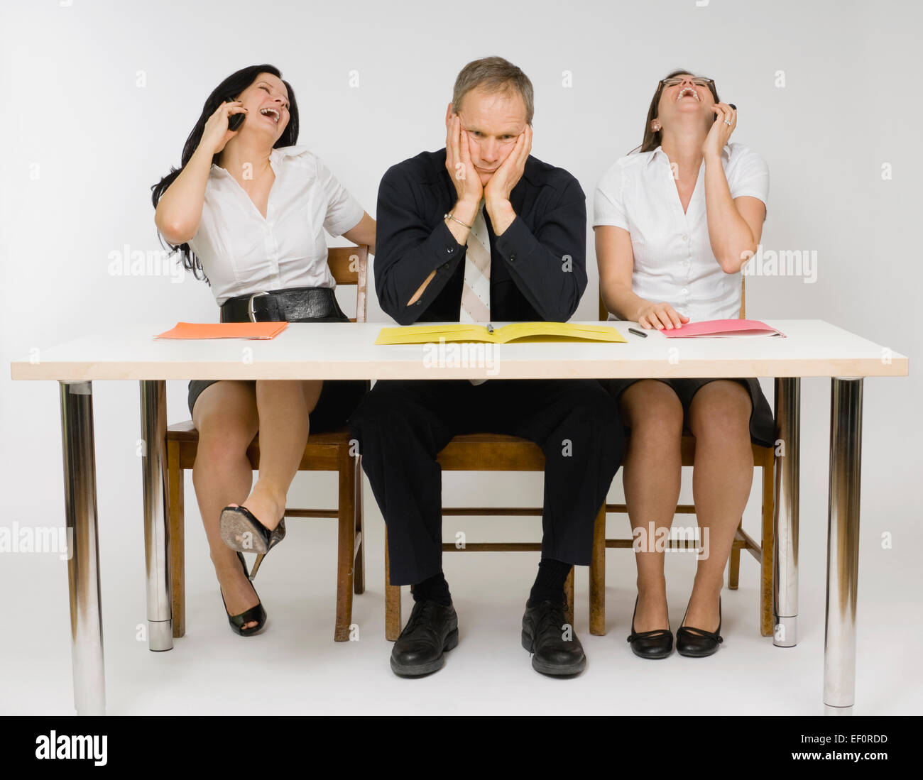 Frustrado hombre sentado en una mesa con mujeres hablando por teléfono Foto de stock