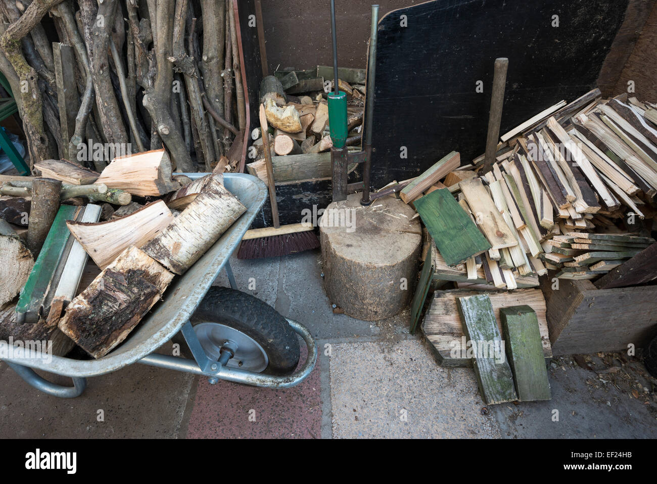 Carretilla de mano llena de troncos al lado de un montón de leña y un registro divisor. Foto de stock
