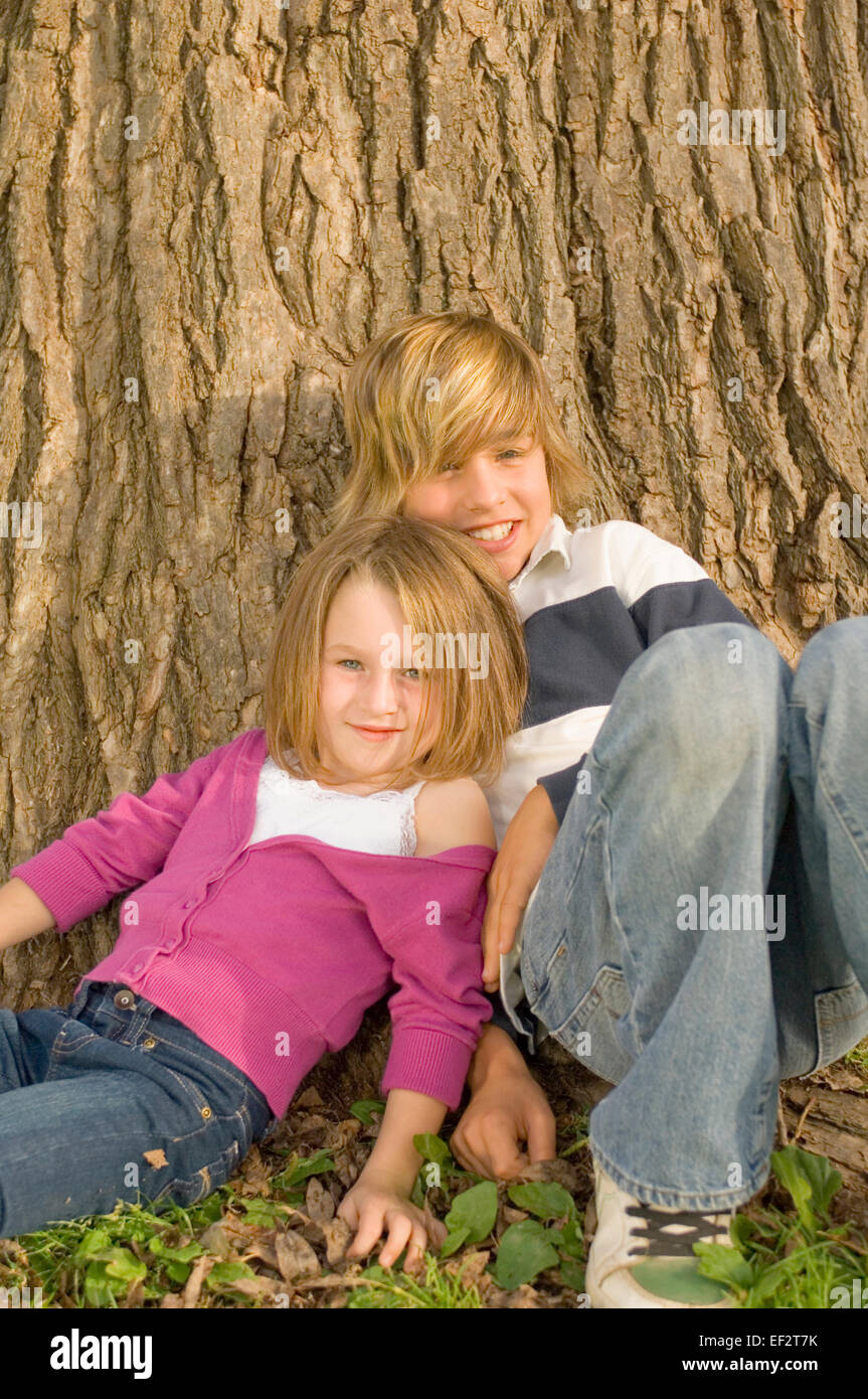 Hermanos inclinada contra un gran tronco de árbol Foto de stock