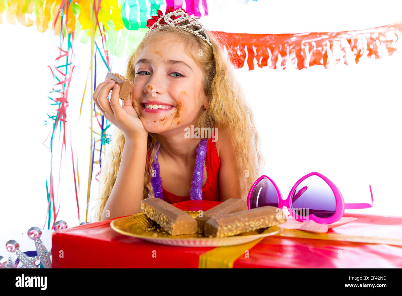 Parte chica feliz con los regalos de cumpleaños comiendo chocolate boca sucia Foto de stock