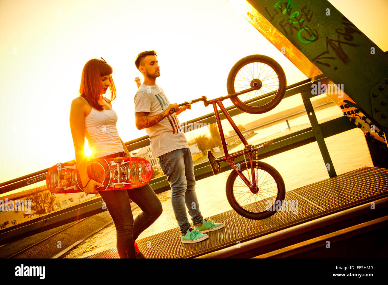Pareja joven con skate y bicicletas BMX afuera Foto de stock