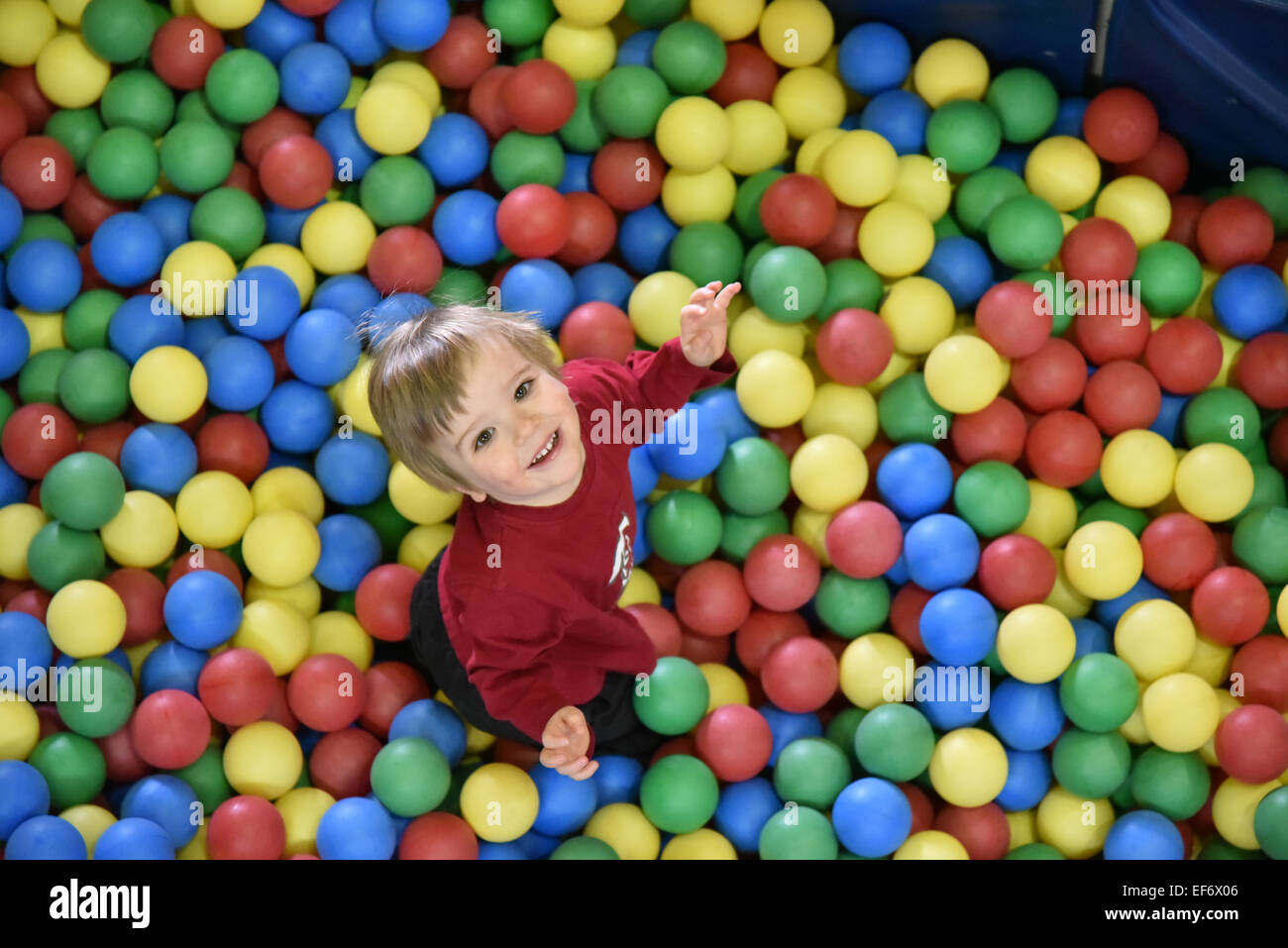 Un niño pequeño (2 1/2 años) sentó en bolas de colores, mirando hacia arriba y sonriendo a la cámara Foto de stock
