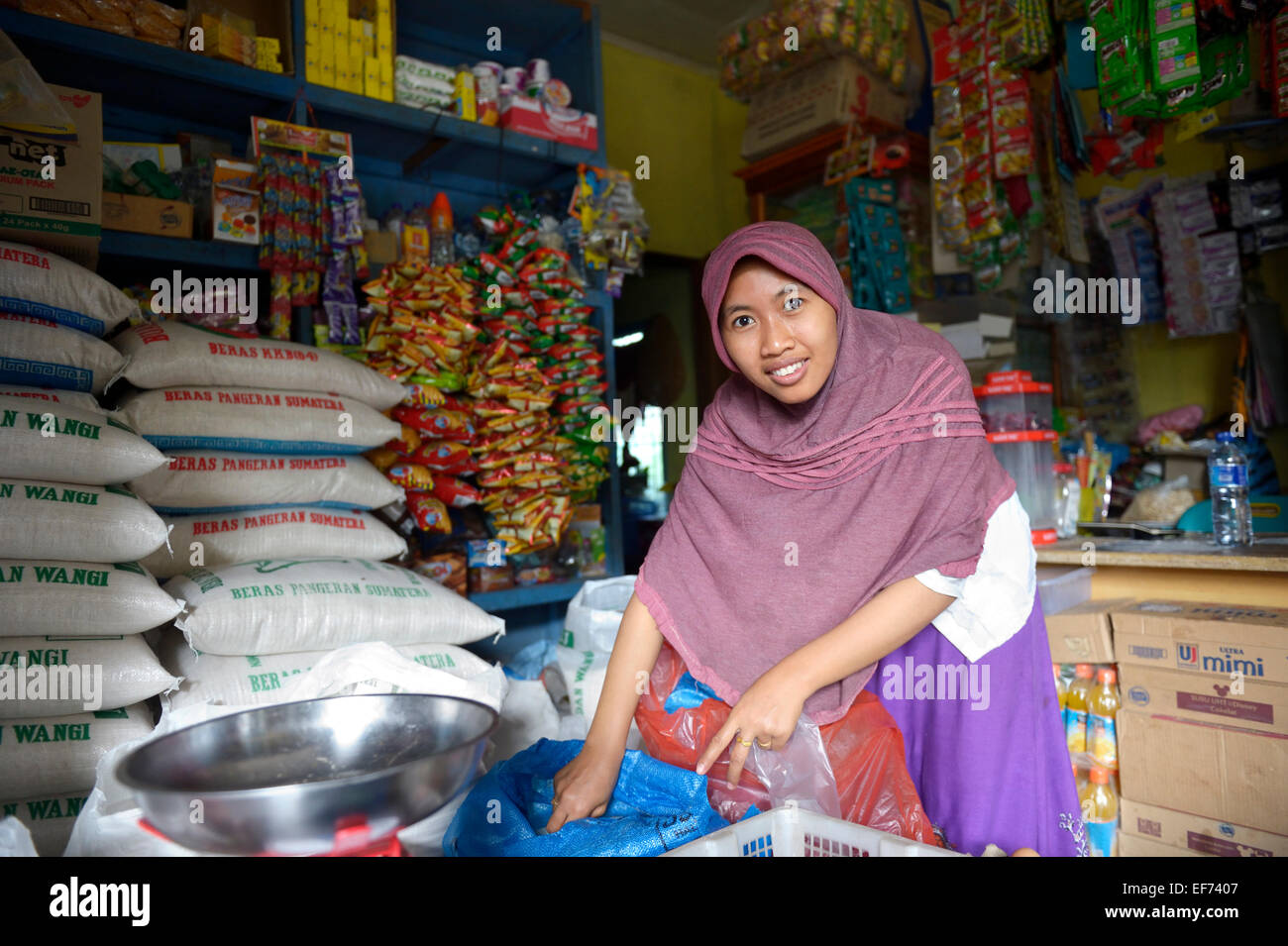Mujer joven con velo, ayudante en una pequeña tienda de comestibles, Lam, subdistrito Rozma Rukam, Aceh, Indonesia Foto de stock