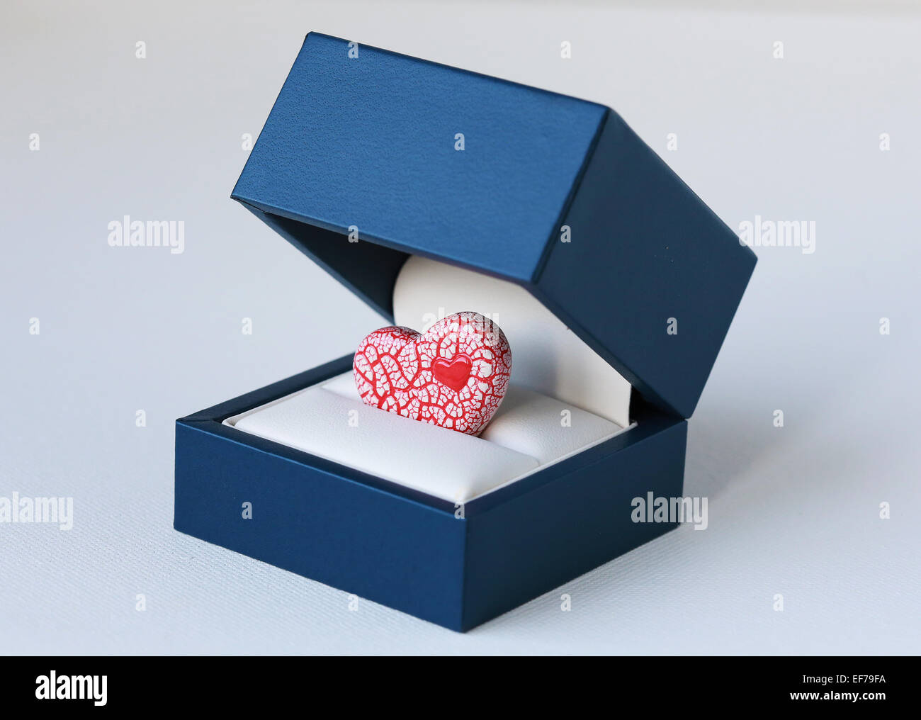 Una imagen de un rojo brillante y blanco corazón de cerámica azul dentro de una caja de joyas, simbolizando una propuesta romántica Foto de stock