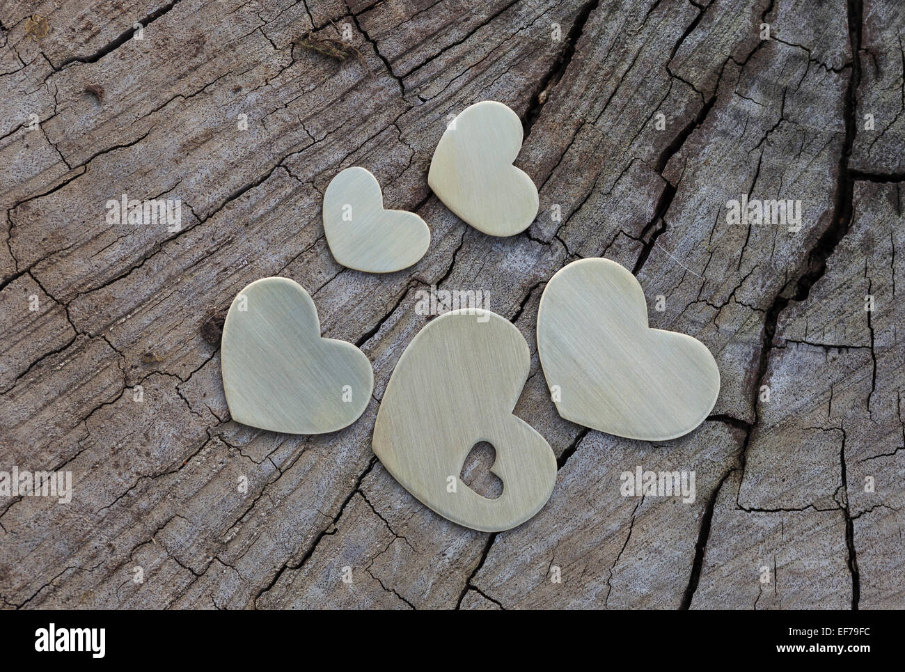 Cinco corazones de metal se colocan en la superficie de madera plana. Foto de stock
