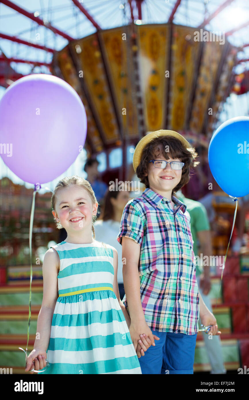 Retrato de chico y chica sujetando globos en el parque de diversiones Foto de stock