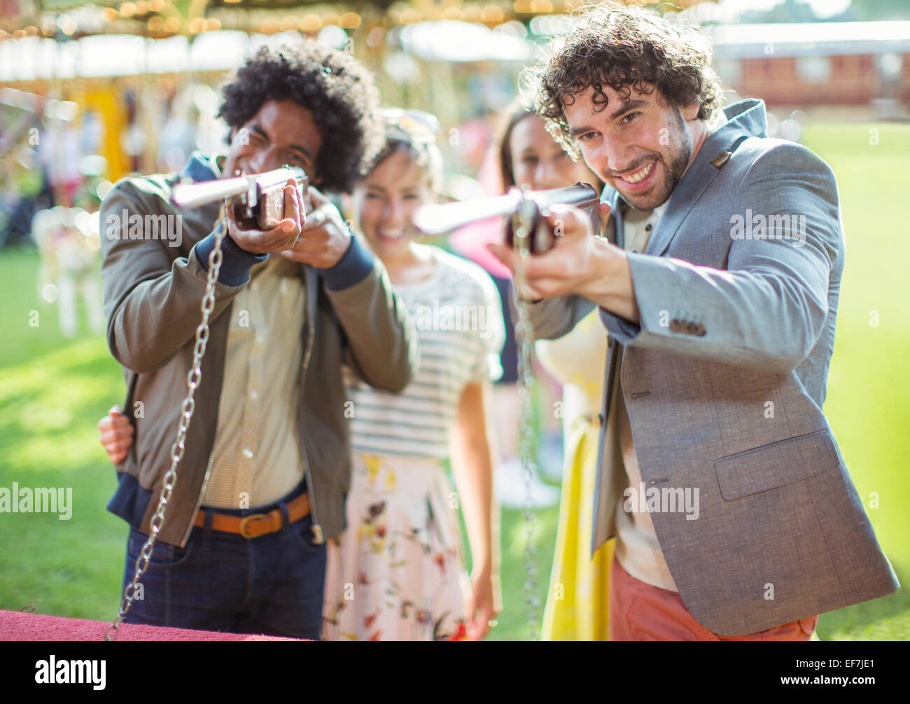 Los hombres jóvenes apuntando con pistolas en parque de diversiones Foto de stock