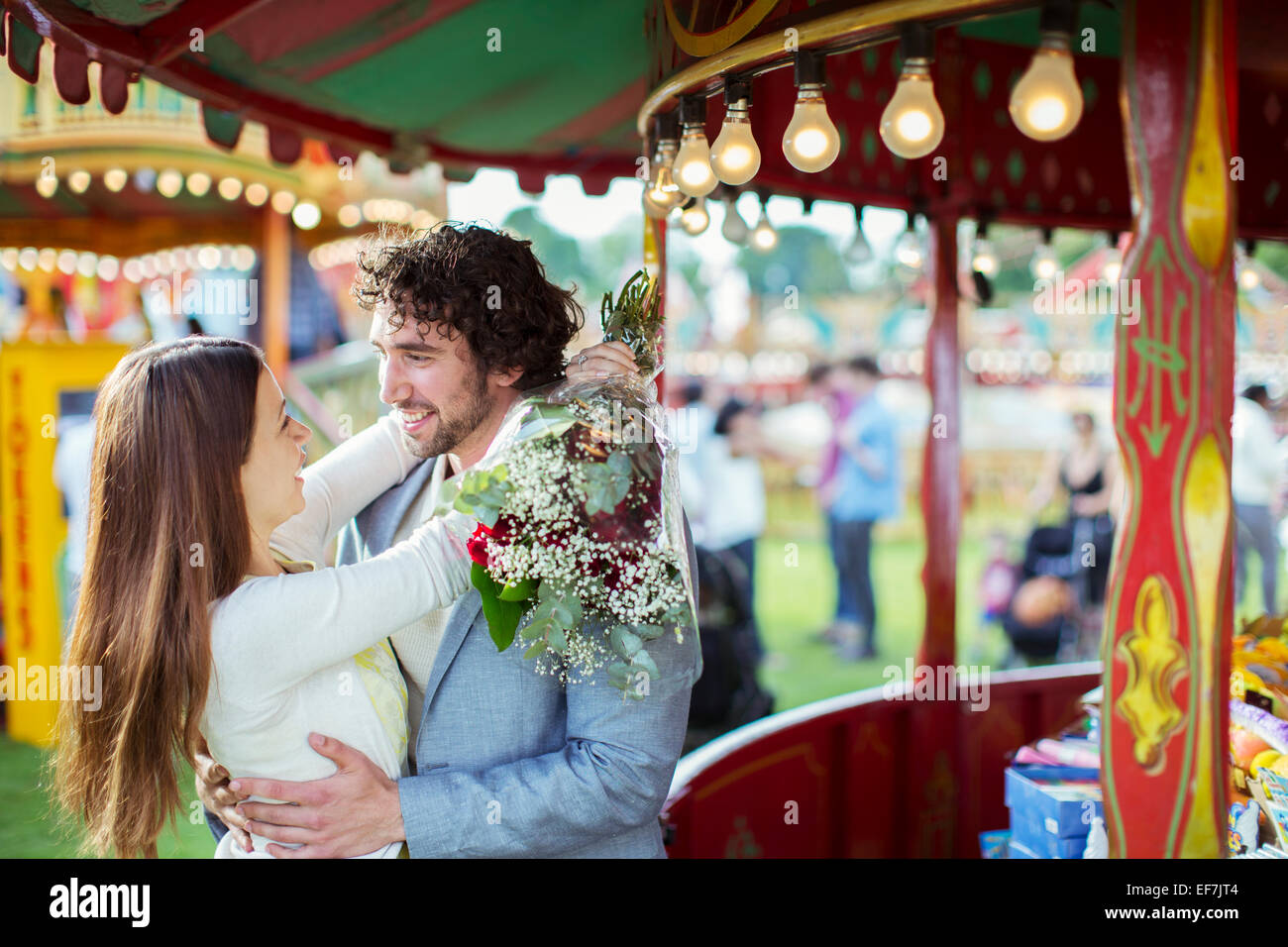 Mujer sosteniendo bouquet y abrazando a su novio en el parque de diversiones Foto de stock