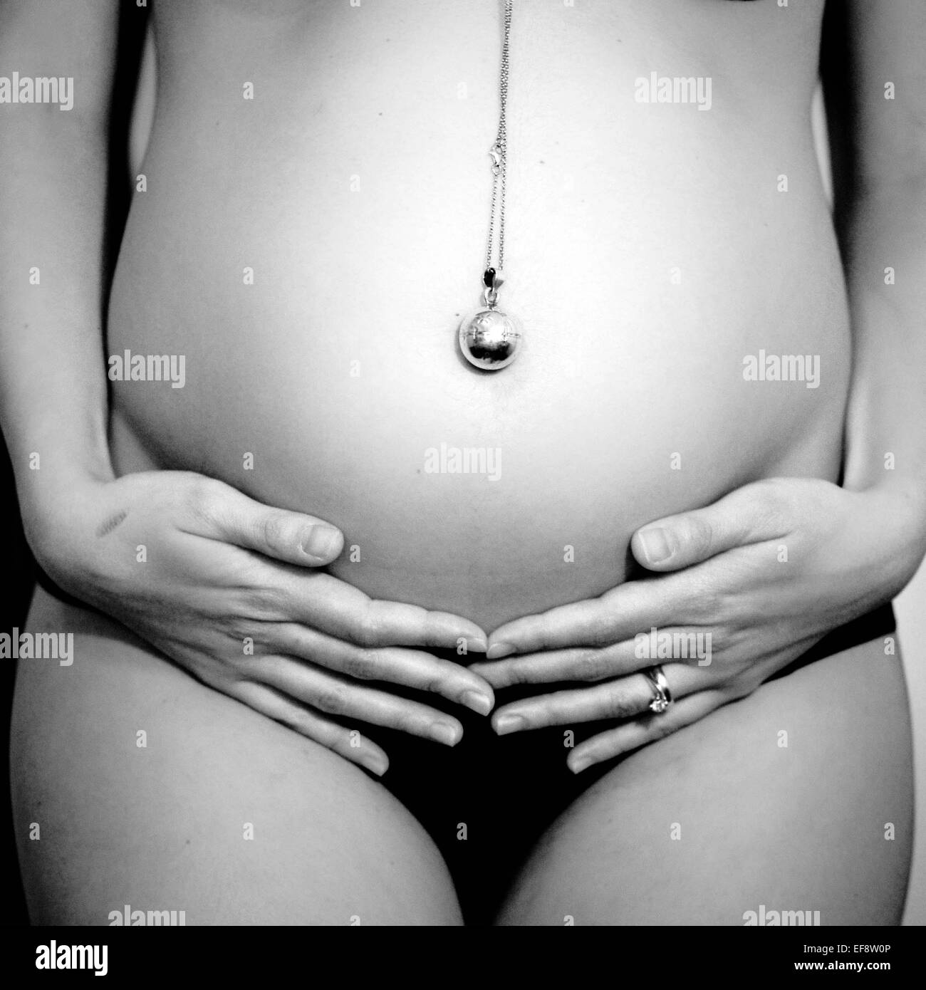 Sección intermedia de mujer embarazada sujetando el vientre vistiendo un  Collar Llamador de angel Fotografía de stock - Alamy