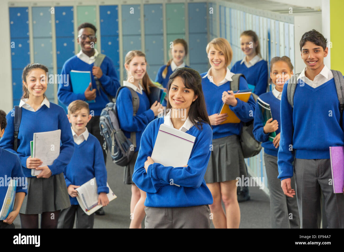 Retrato de grupo de escolares vistiendo uniformes escolares de pie en el pasillo y sonriente Foto de stock