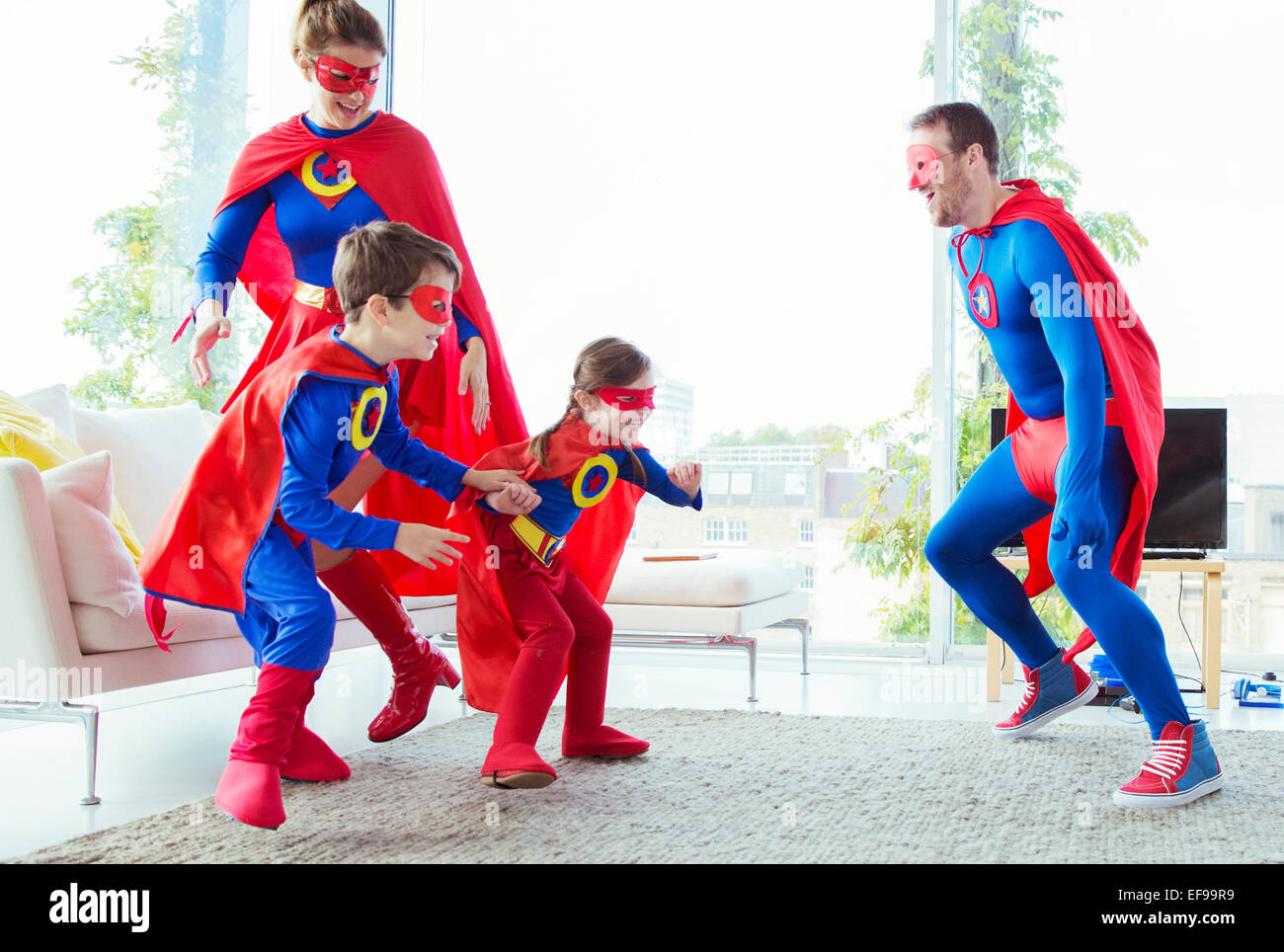 La familia de superhéroes persiguiendo unos a otros en la sala de estar Foto de stock